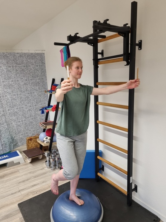 Frau auf Bosu Balancetrainer mit 2 Sticks in der Hand für das neurozentrierte Training